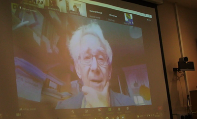 Lord Andrew Stunell on Zoom, projected on the big screen.